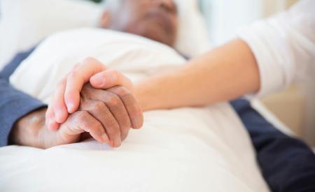 Sick person in bed. Another person is holding their hand.